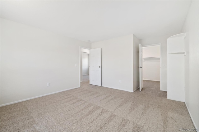 unfurnished bedroom with carpet, a spacious closet, baseboards, and a closet