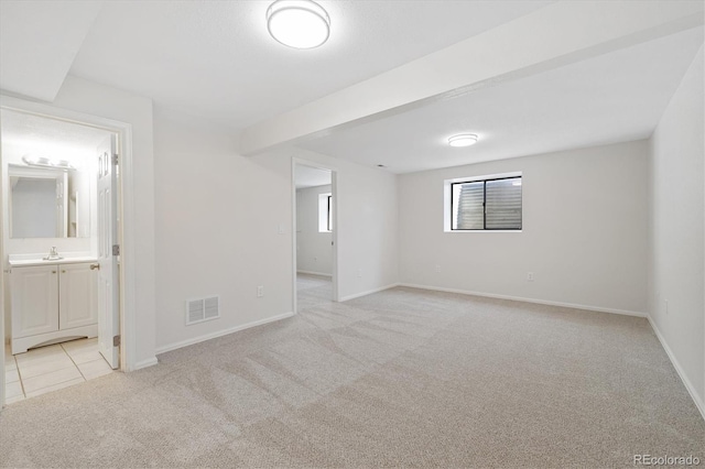 unfurnished bedroom featuring baseboards, visible vents, light colored carpet, ensuite bath, and a sink