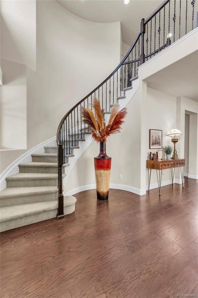 staircase with a towering ceiling, wood finished floors, baseboards, and recessed lighting