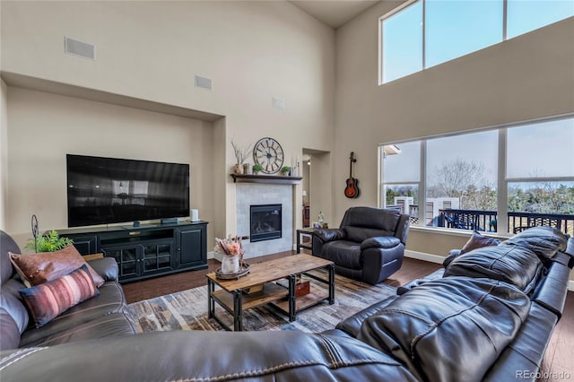living area with healthy amount of natural light, wood finished floors, a high ceiling, and a fireplace
