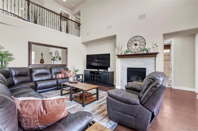 living room with a towering ceiling, a tile fireplace, wood finished floors, and baseboards