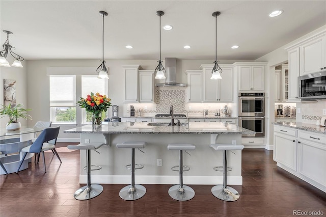 kitchen with stainless steel appliances, wall chimney range hood, tasteful backsplash, a sink, and recessed lighting