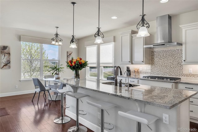kitchen featuring wall chimney exhaust hood, stainless steel gas cooktop, a sink, baseboards, and decorative backsplash