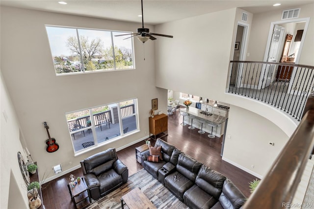 living room with ceiling fan, a towering ceiling, wood finished floors, recessed lighting, and baseboards