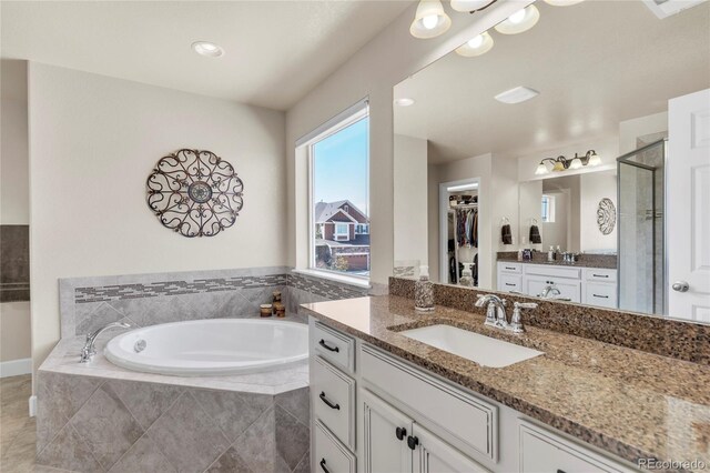 bathroom with a stall shower, a garden tub, two vanities, a walk in closet, and tile patterned floors