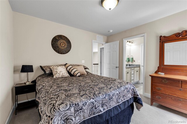 bedroom featuring light colored carpet, baseboards, and ensuite bath