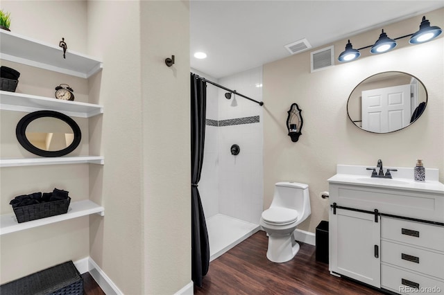 bathroom with toilet, wood finished floors, a tile shower, vanity, and baseboards