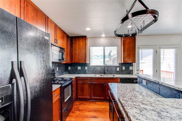 19043 E 58th Ave, Denver, CO 80249 - kitchen with black appliances, light wood-style flooring, a textured ceiling, decorative backsplash, and light stone countertops