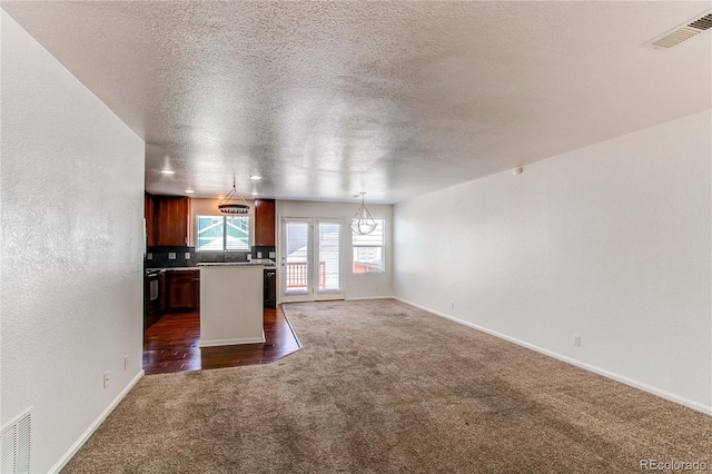 19043 E 58th Ave, Denver, CO 80249 - kitchen featuring dark colored carpet, open floor plan, a textured ceiling, a kitchen island, and decorative light fixtures