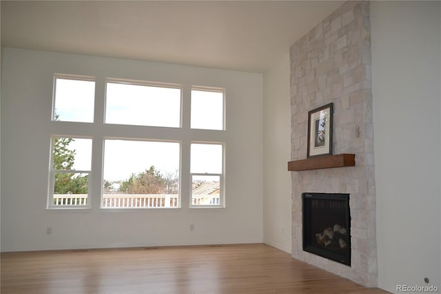 unfurnished living room featuring a high ceiling, a fireplace, wood finished floors, and a healthy amount of sunlight