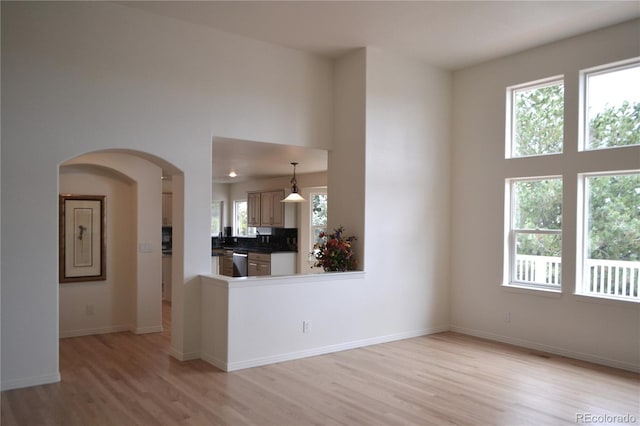 unfurnished living room featuring a towering ceiling, light wood-style flooring, arched walkways, and baseboards