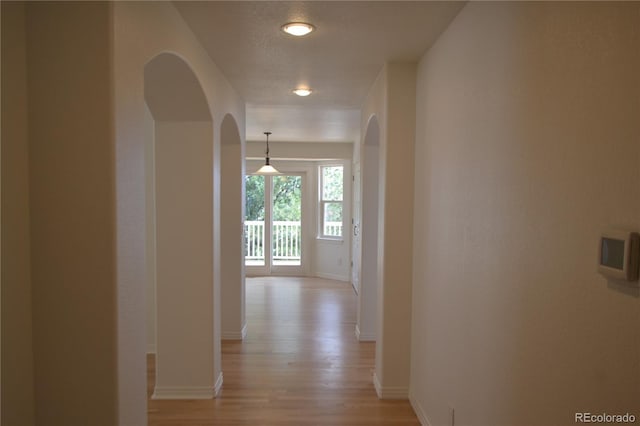 hallway with light wood-style flooring, arched walkways, and baseboards