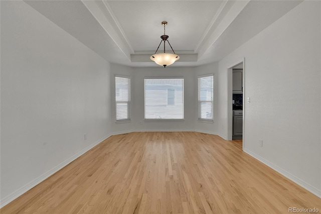 unfurnished room with light wood-style floors, baseboards, and a tray ceiling