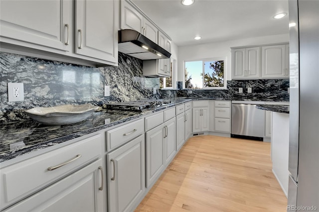 kitchen with light wood-style floors, dark stone countertops, under cabinet range hood, gas stovetop, and stainless steel dishwasher