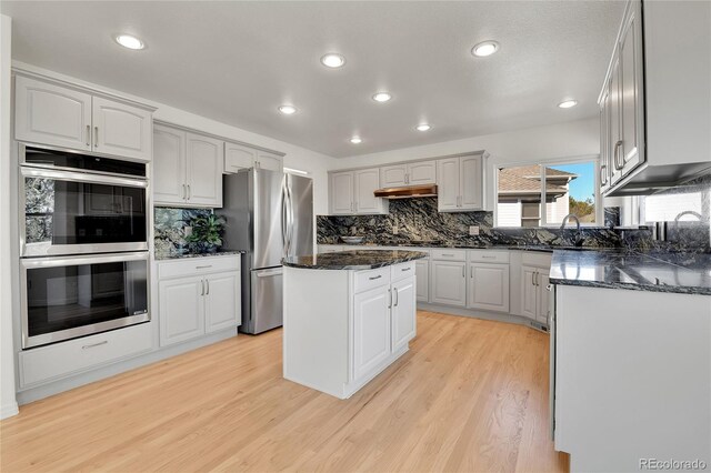 kitchen with a center island, stainless steel appliances, light wood-style floors, dark stone counters, and under cabinet range hood