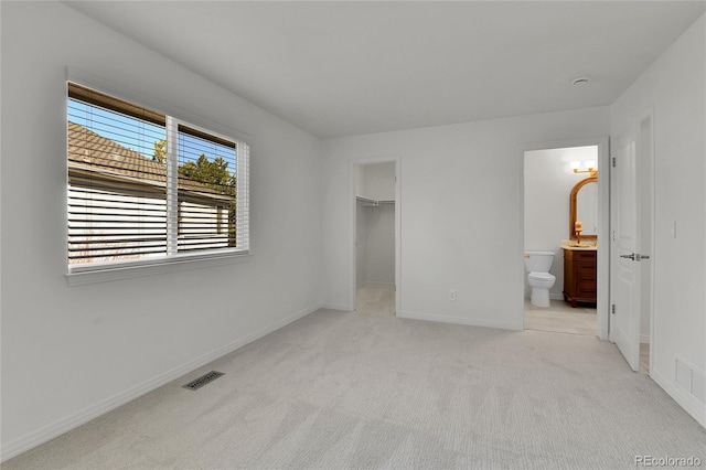 unfurnished bedroom with light carpet, a walk in closet, visible vents, and baseboards