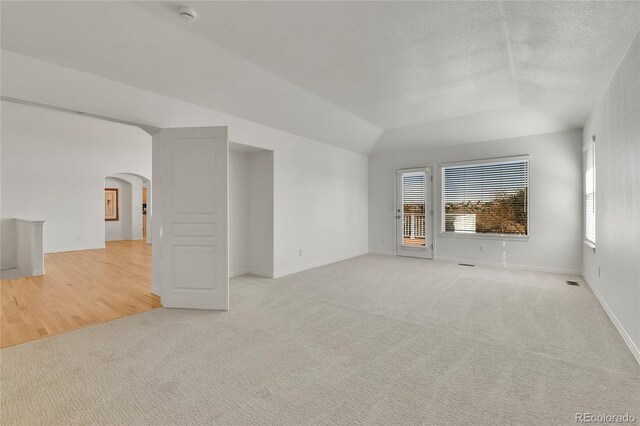 unfurnished room featuring light carpet, arched walkways, vaulted ceiling, and a textured ceiling