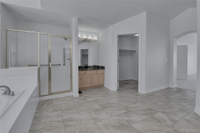 full bathroom featuring a walk in closet, a garden tub, a stall shower, vanity, and baseboards