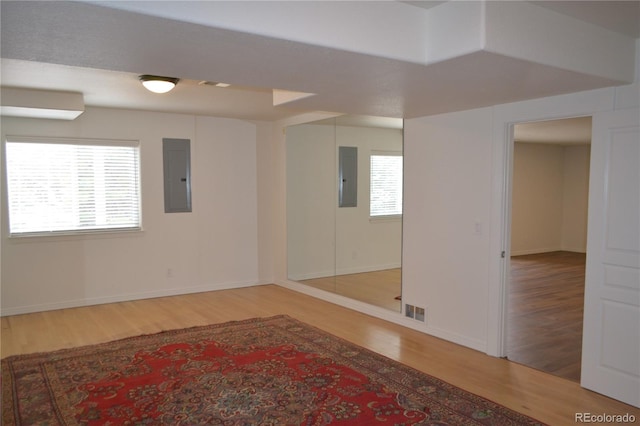 spare room featuring electric panel, visible vents, baseboards, and wood finished floors