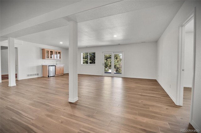 unfurnished living room featuring light wood-style floors, baseboards, wet bar, and visible vents