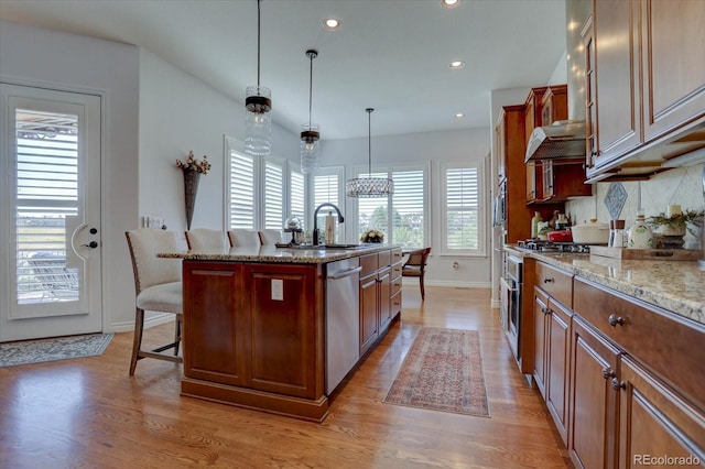 kitchen featuring a wealth of natural light, an island with sink, stainless steel appliances, and decorative light fixtures