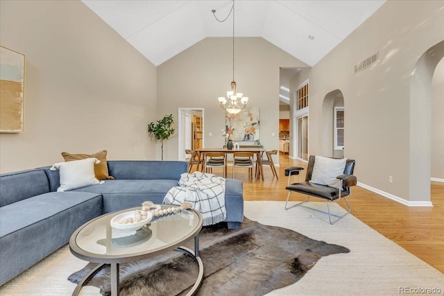 living room with high vaulted ceiling, an inviting chandelier, and light hardwood / wood-style floors