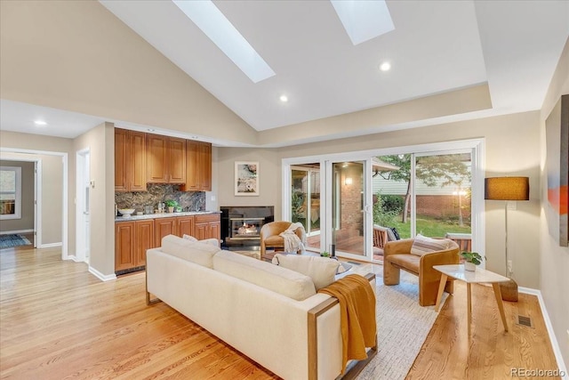 living room with high vaulted ceiling, light hardwood / wood-style floors, and a skylight