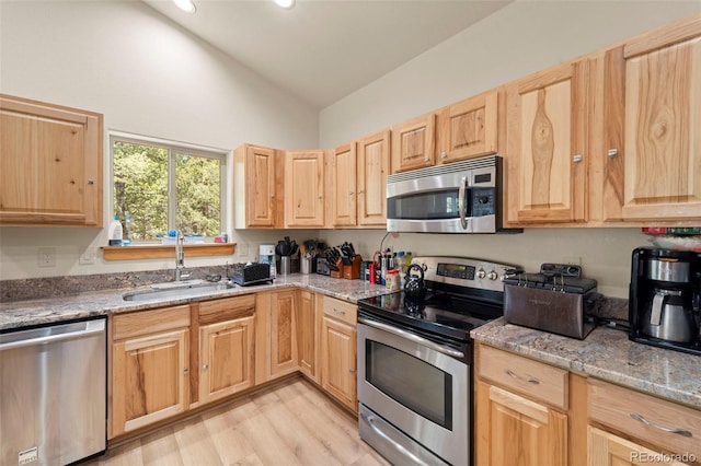 kitchen with light brown cabinetry, light wood-style floors, high vaulted ceiling, a sink, and stainless steel appliances