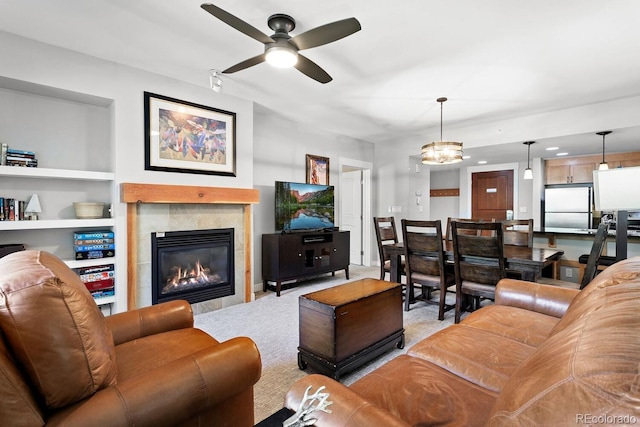 living room featuring ceiling fan with notable chandelier, built in features, and a tile fireplace