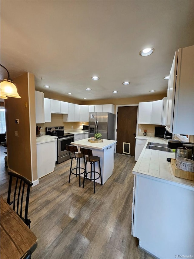 2034 S Truckee St, Aurora, CO 80013 - kitchen featuring appliances with stainless steel finishes, a kitchen island, white cabinetry, dark wood finished floors, and a breakfast bar area
