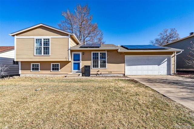 tri-level home with solar panels, an attached garage, concrete driveway, and a front yard