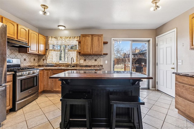 kitchen with gas stove, open shelves, a sink, under cabinet range hood, and a kitchen breakfast bar