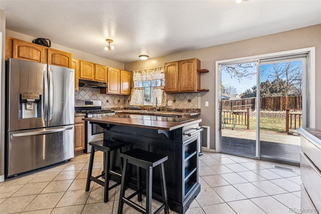 kitchen with under cabinet range hood, light tile patterned floors, decorative backsplash, appliances with stainless steel finishes, and open shelves