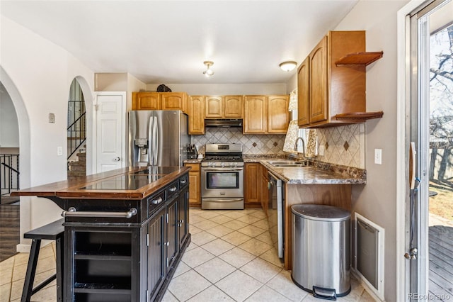 kitchen featuring a sink, open shelves, under cabinet range hood, dark countertops, and appliances with stainless steel finishes