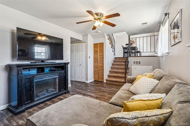 living area with dark wood-style floors, visible vents, stairs, and a glass covered fireplace