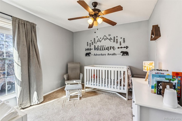 carpeted bedroom with baseboards, a nursery area, and a ceiling fan