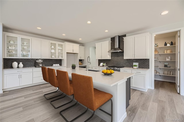 kitchen with wall chimney range hood, a kitchen breakfast bar, a center island with sink, and stainless steel stove