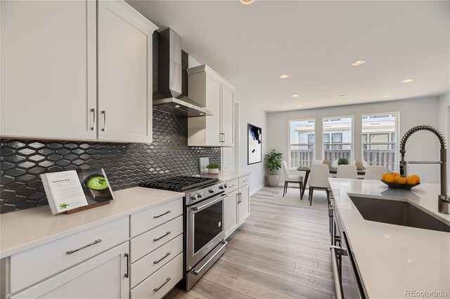 kitchen featuring light hardwood / wood-style flooring, sink, stainless steel range, wall chimney range hood, and white cabinets