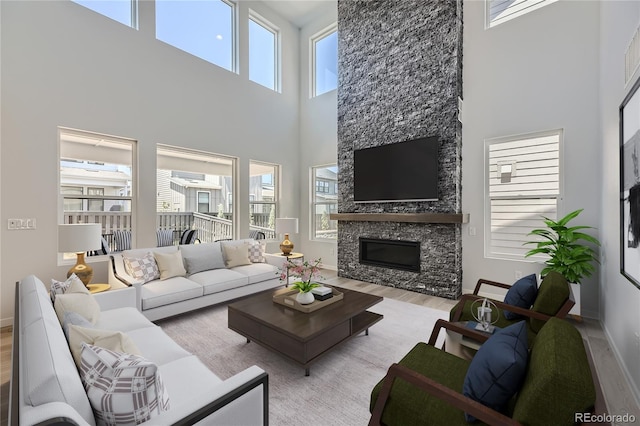 living room featuring light hardwood / wood-style floors, a towering ceiling, and a stone fireplace