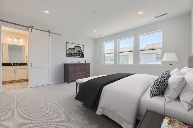 bedroom with a barn door, light colored carpet, visible vents, and recessed lighting