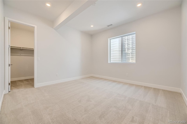 unfurnished bedroom with a walk in closet, beam ceiling, a closet, and light carpet