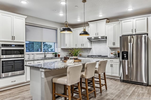 kitchen with light stone countertops, stainless steel appliances, decorative light fixtures, a kitchen island, and light wood-type flooring