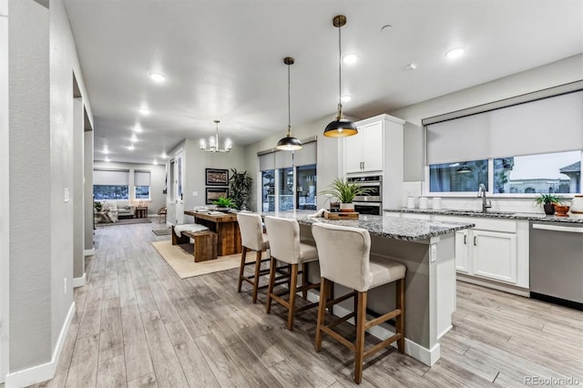 kitchen with a center island, white cabinets, hanging light fixtures, light stone countertops, and stainless steel appliances