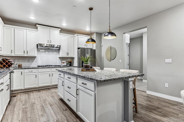 kitchen with appliances with stainless steel finishes, white cabinets, a center island, light hardwood / wood-style floors, and hanging light fixtures