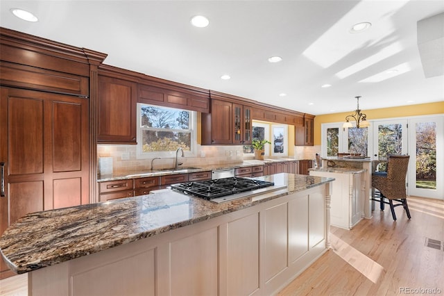 kitchen featuring sink, decorative light fixtures, appliances with stainless steel finishes, a kitchen island, and light stone countertops