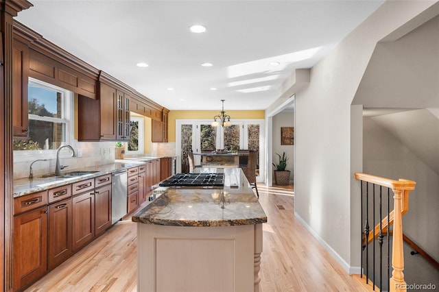 kitchen featuring decorative light fixtures, sink, dark stone counters, a center island, and stainless steel dishwasher