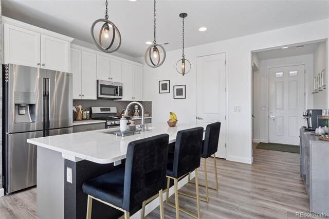 25106 E 1st Ave, Aurora, CO 80018 - kitchen featuring appliances with stainless steel finishes, recessed lighting, light wood-style floors, decorative backsplash, and an island with sink