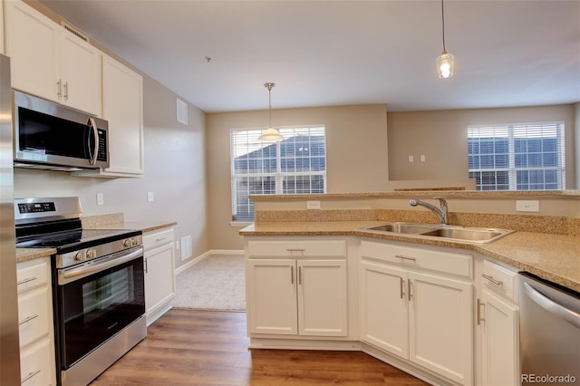 kitchen featuring stainless steel appliances, sink, light hardwood / wood-style floors, white cabinetry, and hanging light fixtures