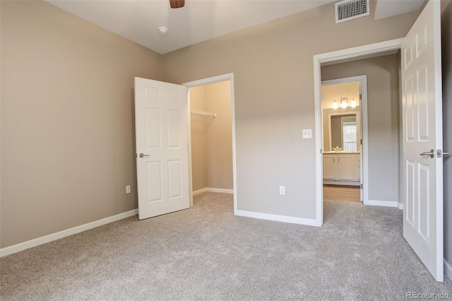 unfurnished bedroom with a walk in closet, ceiling fan, a closet, and light colored carpet