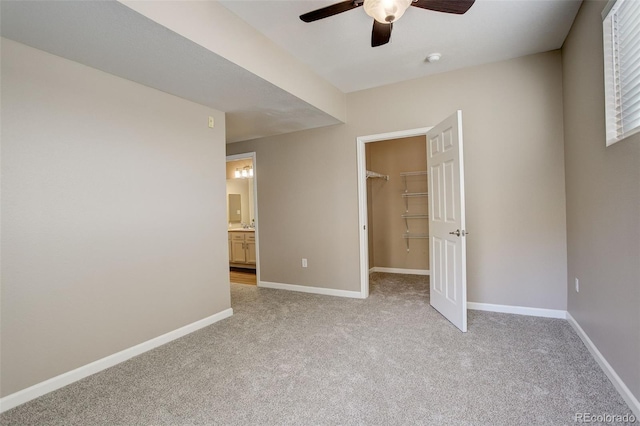 unfurnished bedroom featuring ceiling fan, ensuite bathroom, a walk in closet, light carpet, and a closet